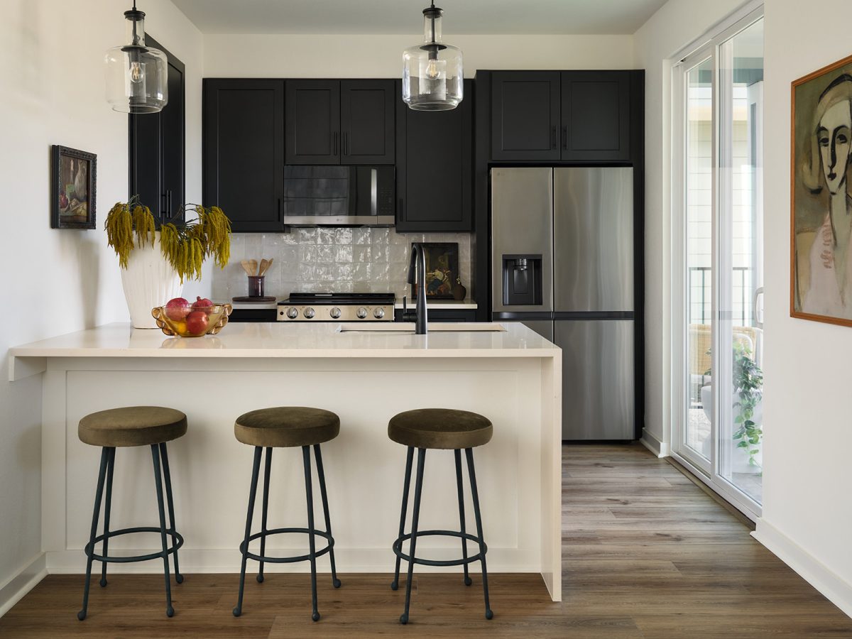 Modern kitchen in Drew Lane model home with black cabinetry, white island, pendant lighting, and warm wood flooring