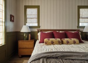 Cozy bedroom with green paneled walls, layered textiles, and warm wood furniture in Drew Lane model home