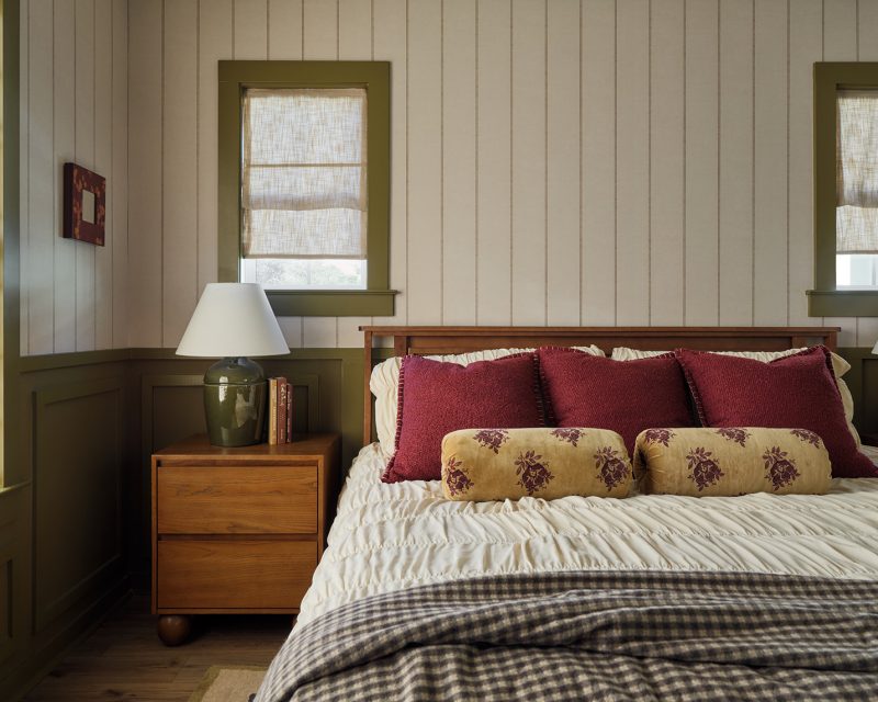 Cozy bedroom with green paneled walls, layered textiles, and warm wood furniture in Drew Lane model home